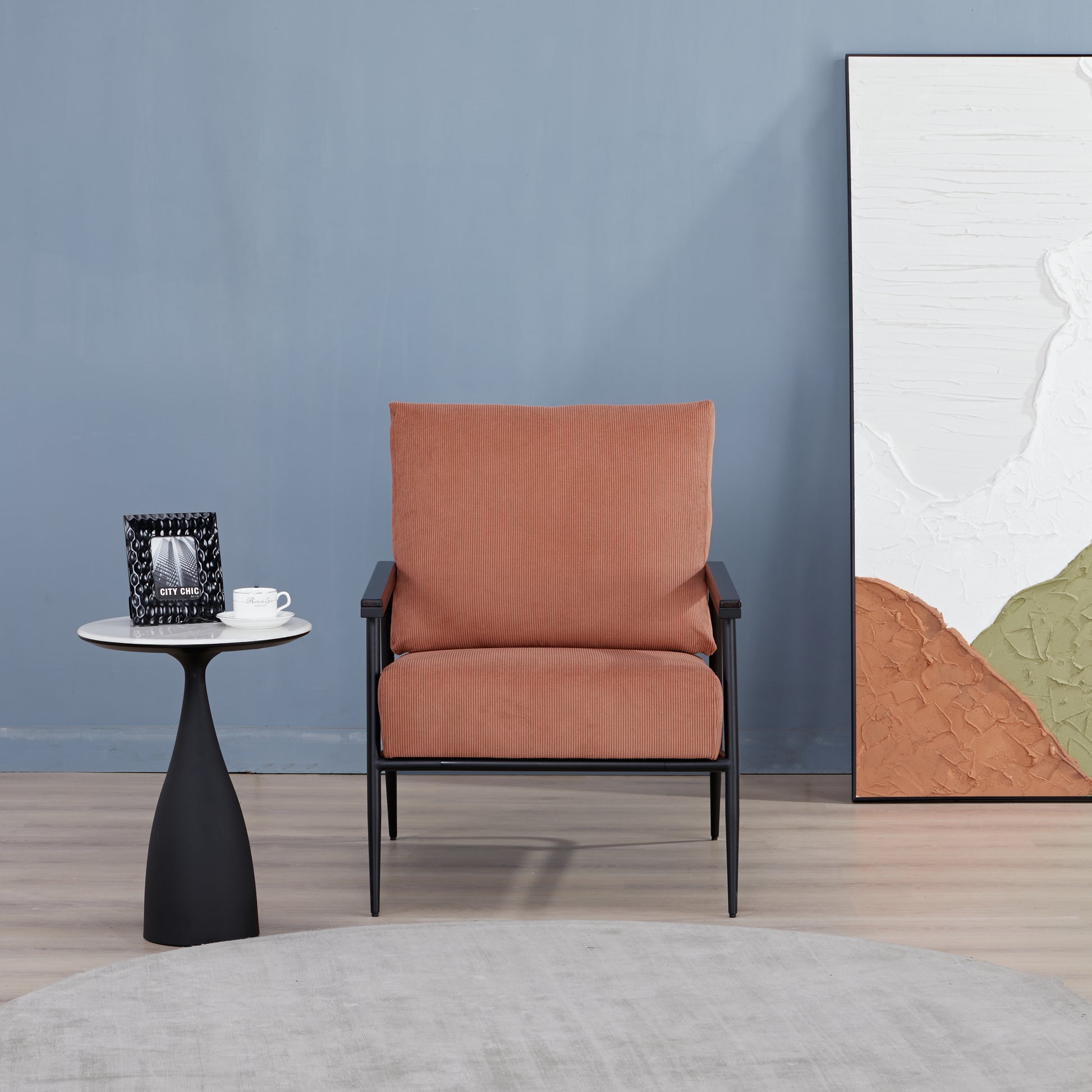 Parker Accent Chair in Corduroy Orange displayed in a modern room with a side table, blue wall, abstract artwork, and ribbed orange upholstery