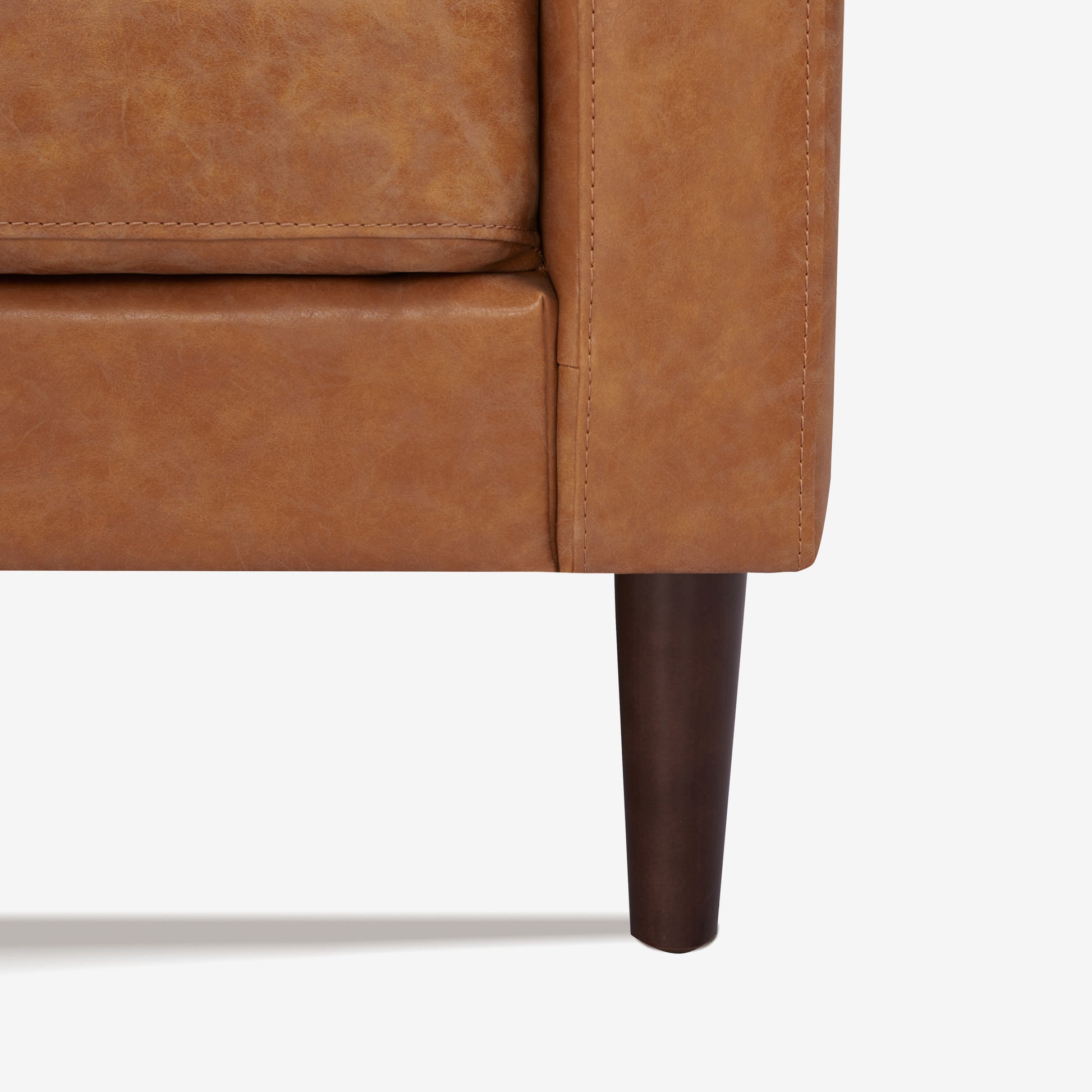 Orlando Loveseat in Faux Leather Camel featuring a close-up of the distressed upholstery, stitched cushion edge, track arm seam, and tapered dark brown leg.