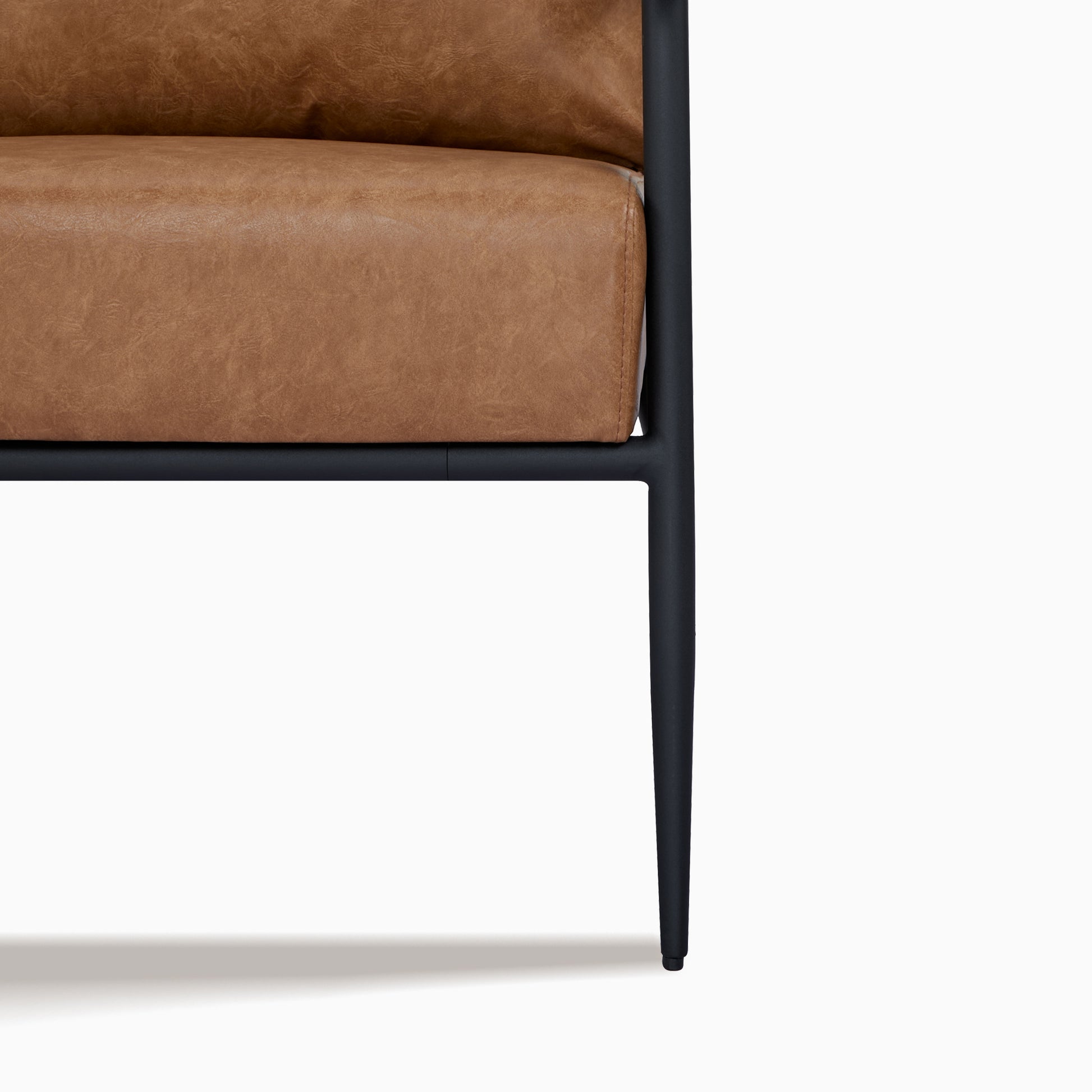 Parker Accent Chair in Faux Leather Light Brown featuring a close-up of the mottled upholstery, stitched edge, black seat support, frame joint, and tapered metal leg