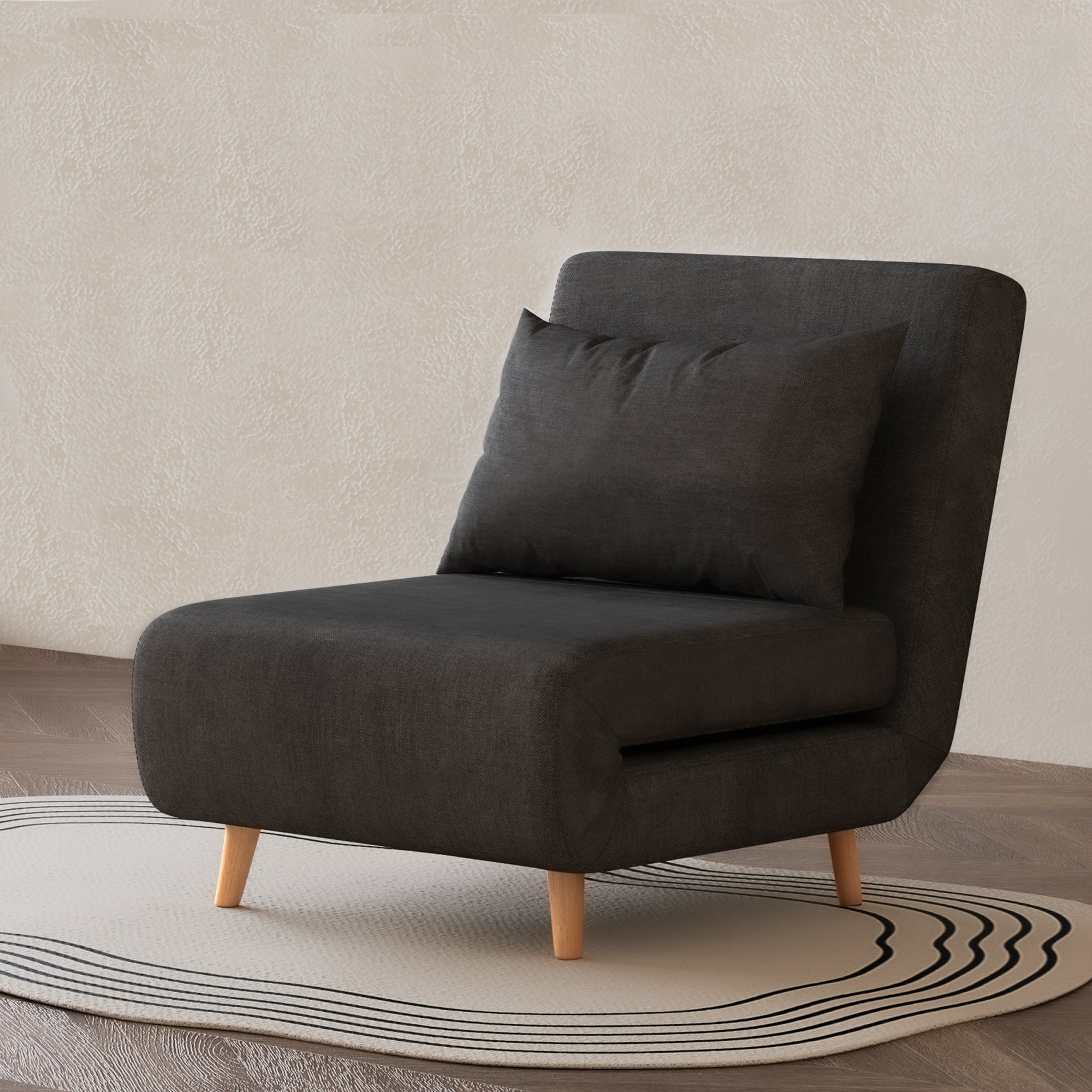 Tustin Convertible Chair in Charcoal styled on a patterned rug with an armless silhouette, matching lumbar pillow, rounded seat, and tapered natural wood legs.